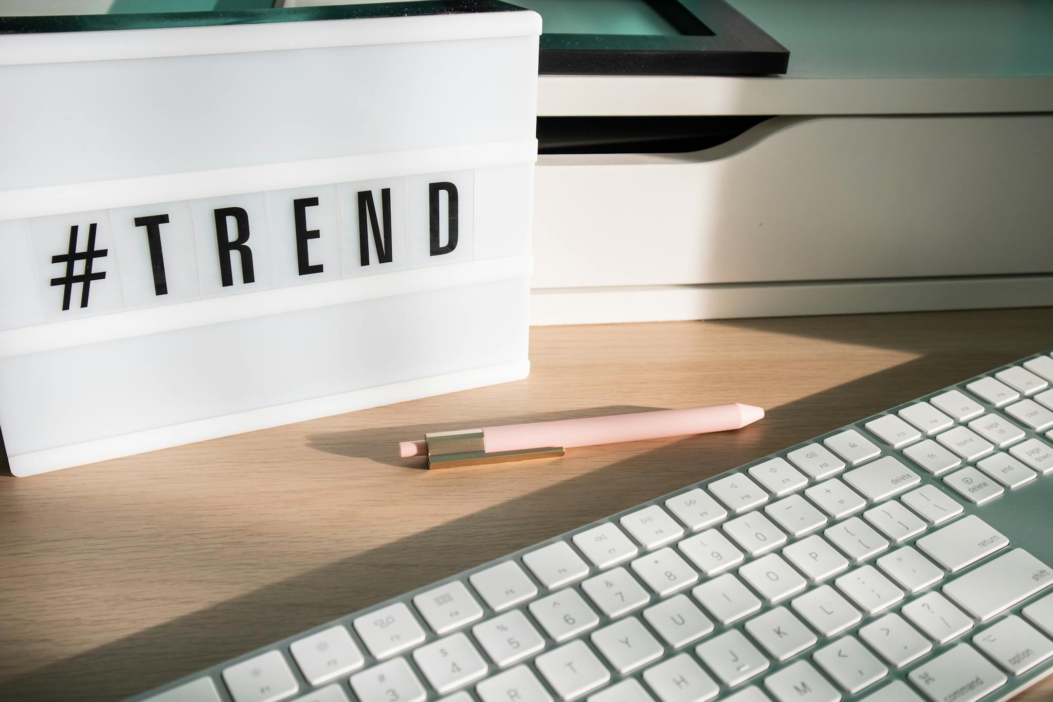 Contemporary workspace featuring a light box showing '#trend,' a pink pen, and a keyboard.